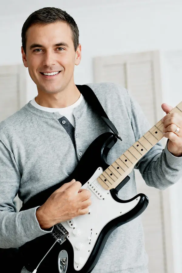 Smiling man in a grey jumper holding a black electric guitar