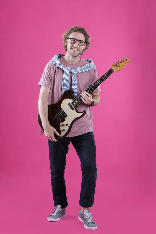 Smiling man holding an electric guitar against a pink background