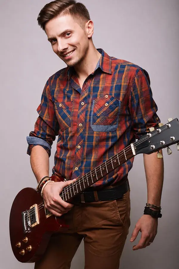 Smiling man in a plaid shirt holding a red electric guitar