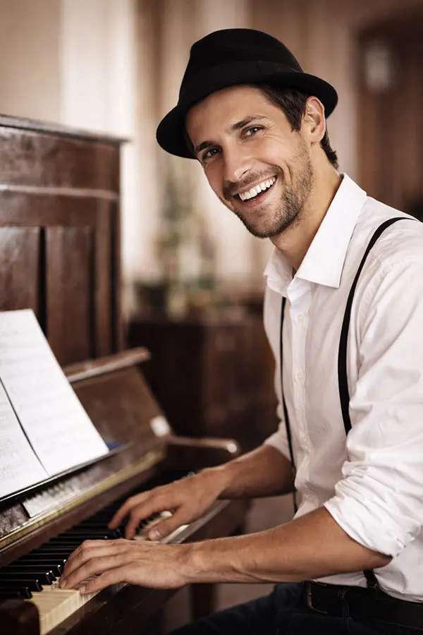 Smiling man in a hat playing piano beside sheet music