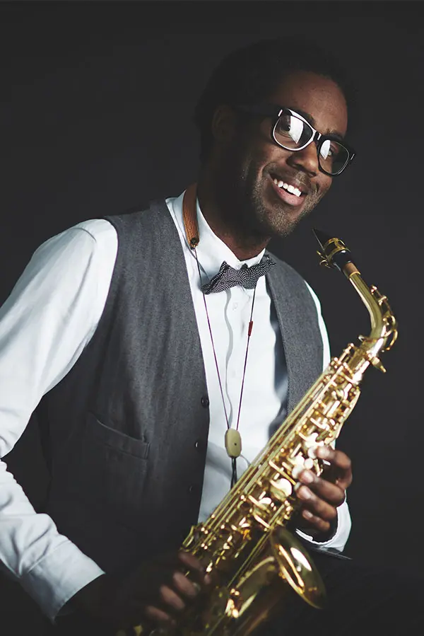 Smiling man in glasses and a waistcoat holding an alto saxophone