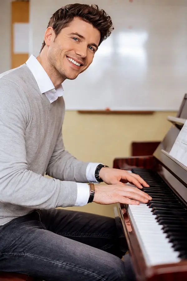 Smiling man seated at a piano with hands on keys