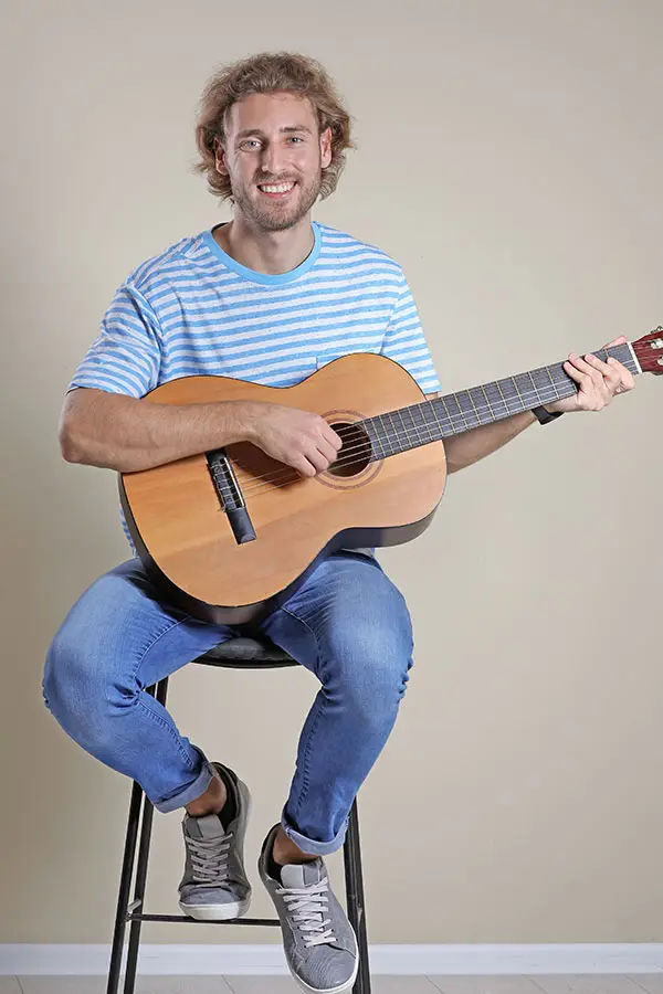 Smiling man in a striped shirt seated with a classical guitar