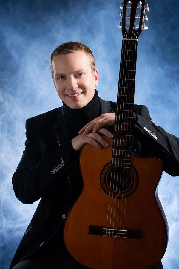 Smiling man in a suit holding a classical guitar