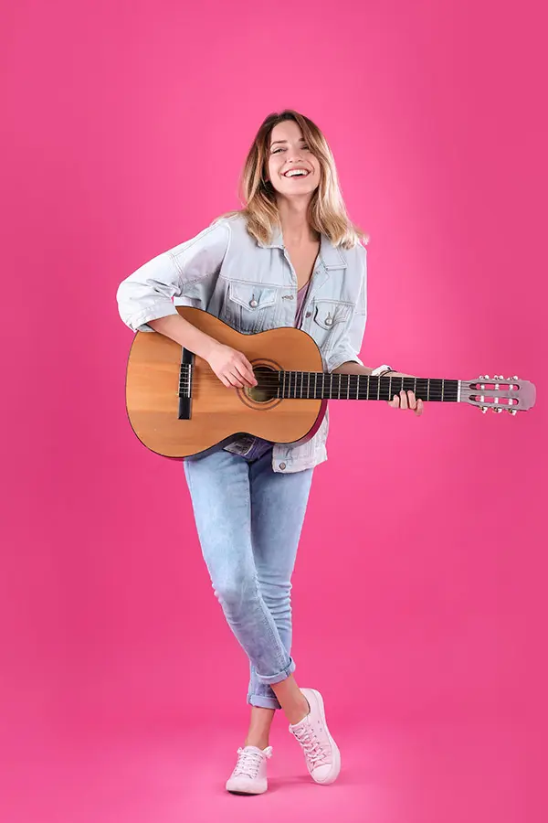 Smiling woman holding a classical guitar against a pink background