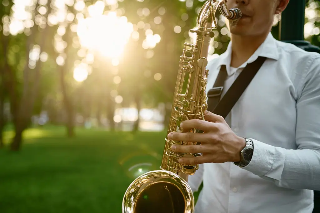 Man playing saxophone in a park with low sunlight