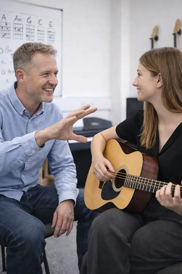 Teacher guiding a woman holding an acoustic guitar