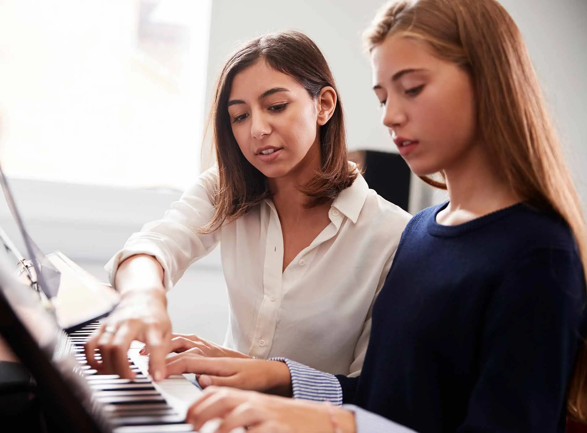 Female student playing the piano with her teacher