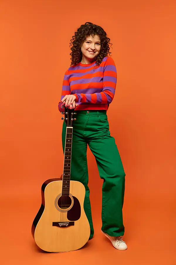 Woman posing with an acoustic guitar on an orange background