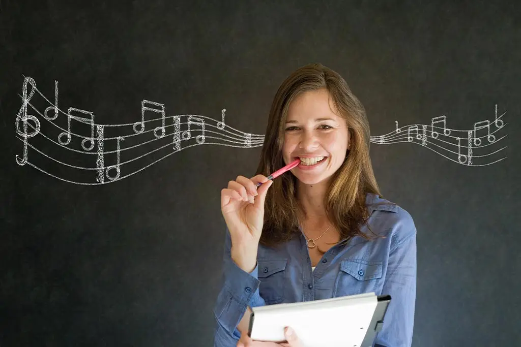 Woman biting a pen while holding a notebook before a chalkboard with music notation