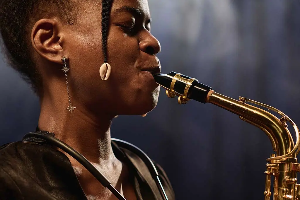 Woman with braided hair playing a saxophone under stage lights
