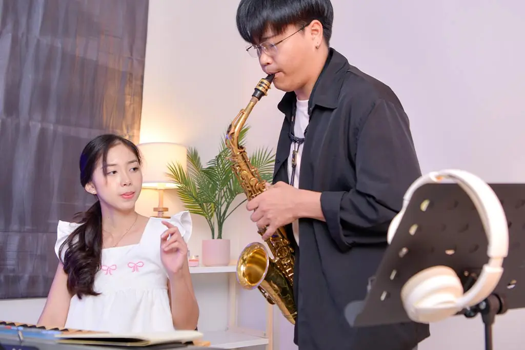 Seated woman guiding a man playing alto saxophone indoors