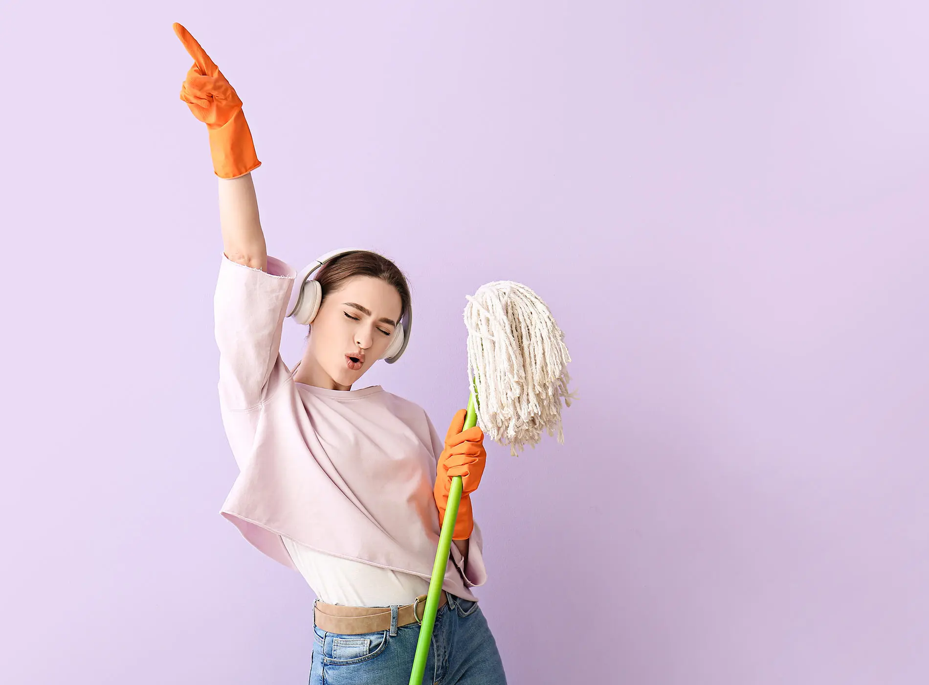 Young woman holding a floor mop and wearing a cleaning gloves listening to music with headphones on