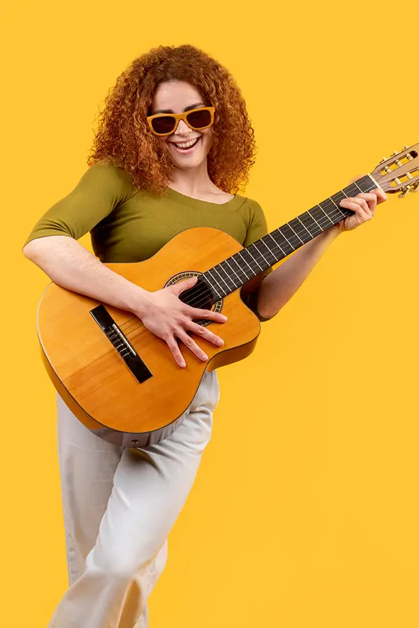 Woman in sunglasses holding a classical guitar against a yellow background