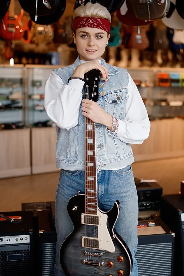 Woman in a denim vest holding an electric guitar in a music shop