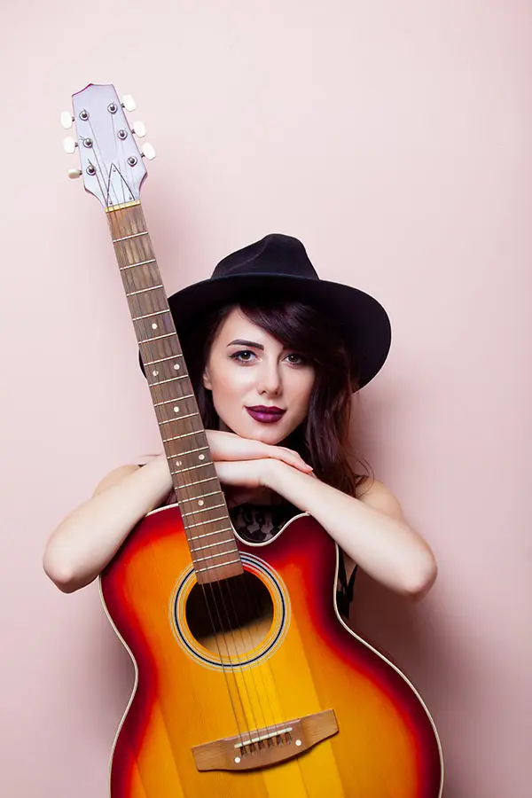 Woman in a black hat holding a sunburst acoustic guitar