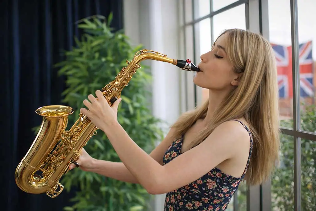 Woman in a floral dress playing alto saxophone beside a window