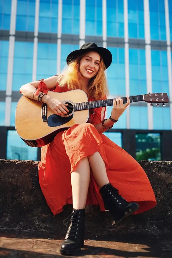 Woman in an orange dress playing acoustic guitar outdoors