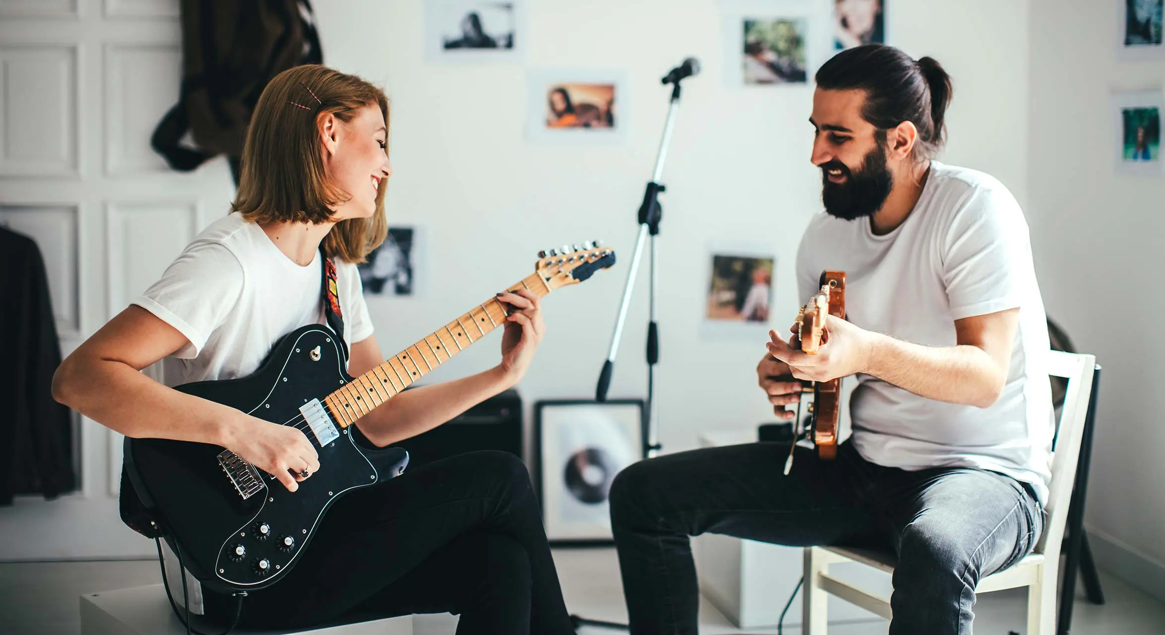 Woman playing a black electric guitar opposite a man holding another guitar