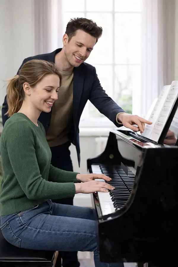 Woman playing a grand piano as a man points at sheet music
