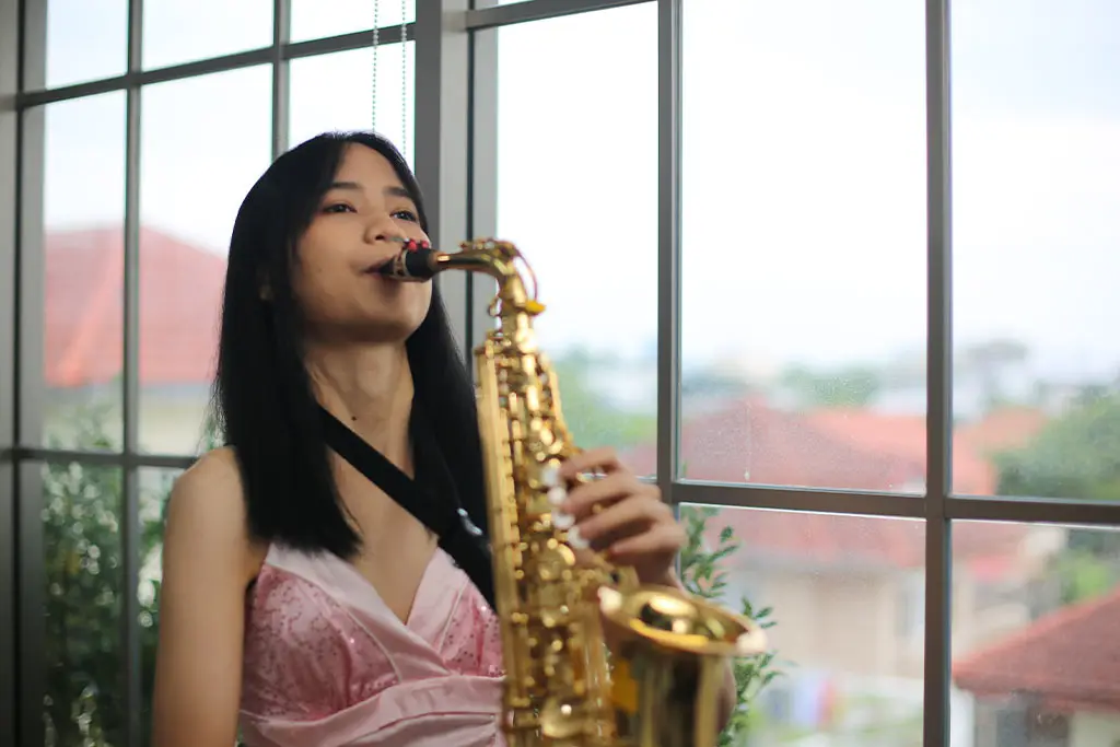 Young woman playing saxophone beside large windows