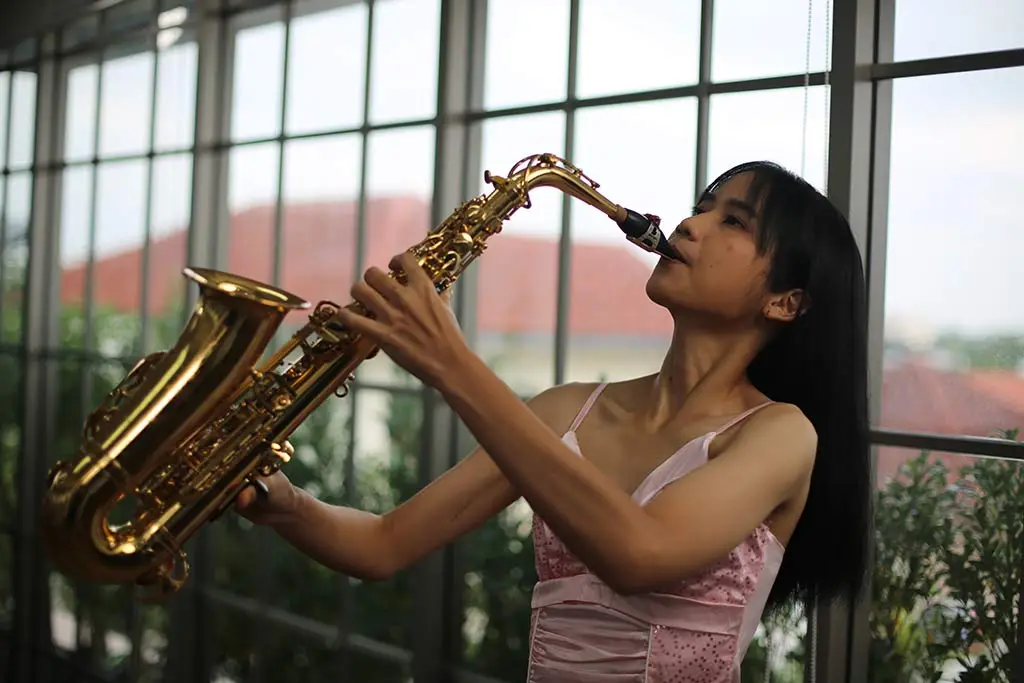 Young woman playing saxophone by large windows