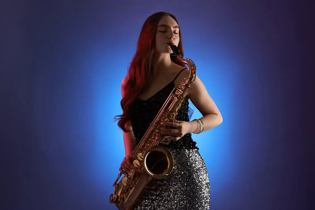 Woman playing a tenor saxophone against a blue studio backdrop