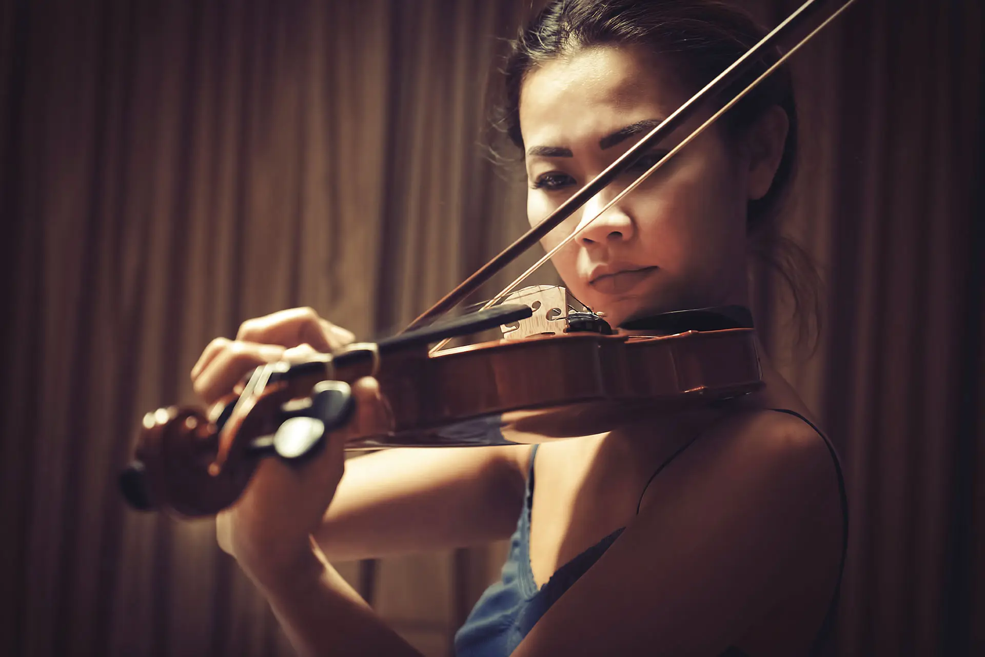 Asian lady playing the violin in a focused manner