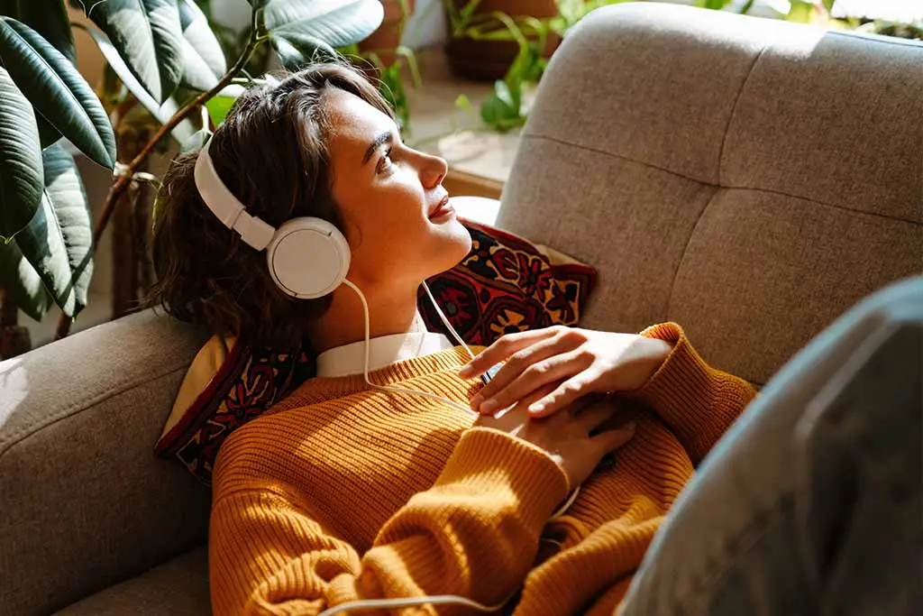 Woman in an orange jumper relaxing with wired headphones on a sofa