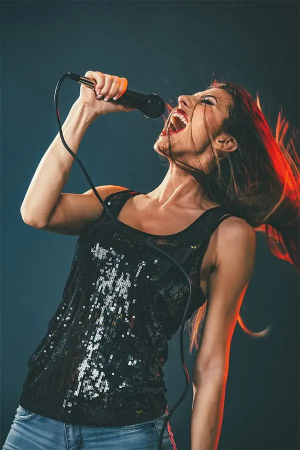 Woman in a sequinned top singing forcefully into a handheld microphone