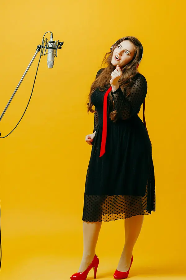 Woman singing into a studio microphone against a yellow background