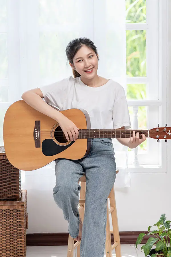 Smiling woman seated by a window with an acoustic guitar