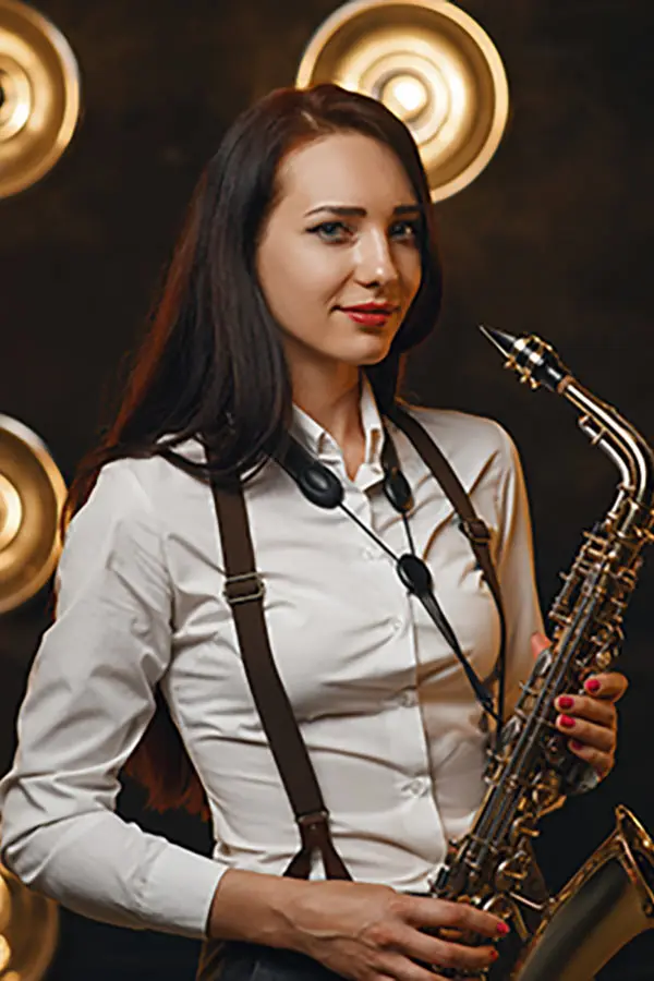 Woman in a white shirt holding a saxophone before stage lights