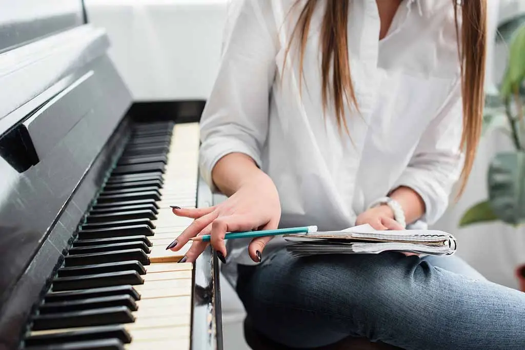Woman holding a pencil and notebook beside piano keys