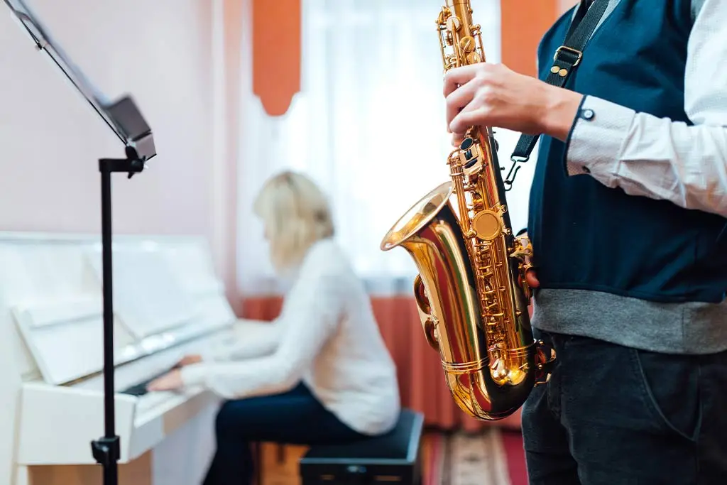 Young boy playing saxophone while teacher plays piano