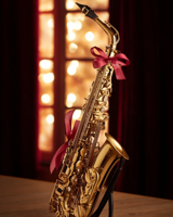 An alto saxophone with a red bow in front of a glowing window