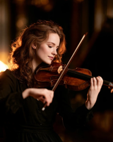A woman with long auburn hair playing the violin, eyes on the instrument