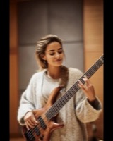 A smiling woman playing a five-string bass guitar